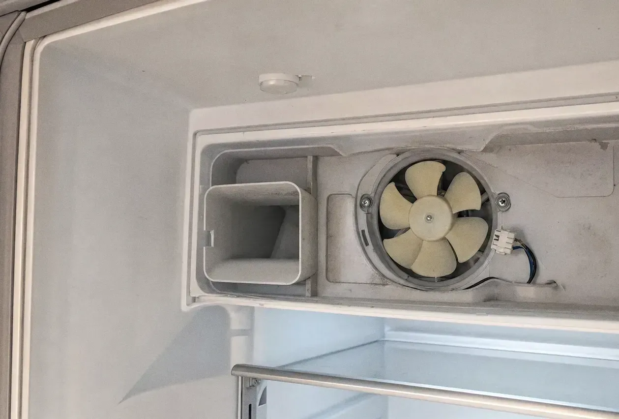 Interior of a cold compartment showing the circular circulation fan behind its grille beside a moulded bin housing